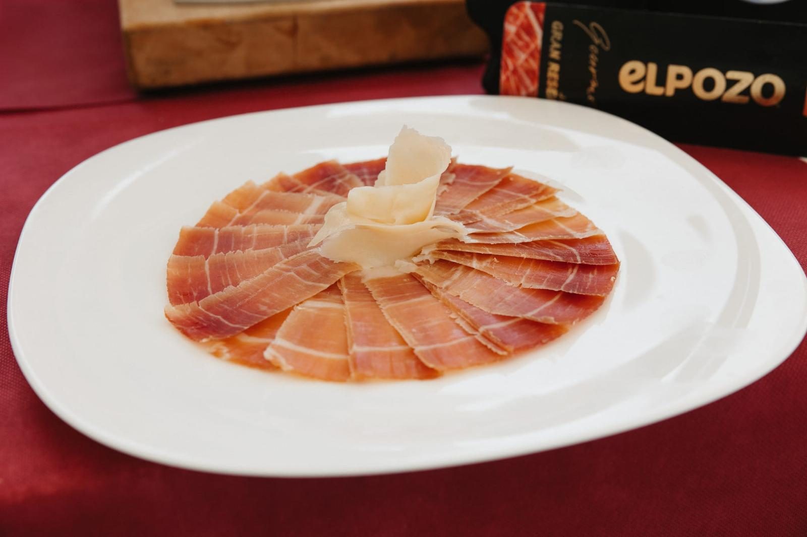 Plato de jamón ibérico con queso curado servido en una mesa con mantel granate