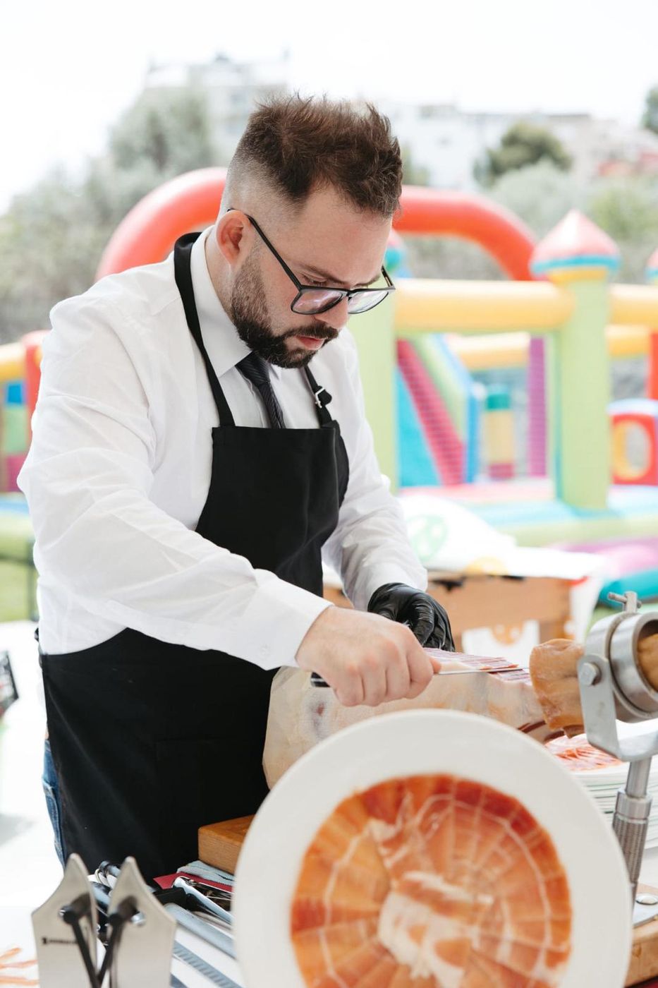 Adrián cortando jamón ibérico de pie en un evento al aire libre con guantes negros