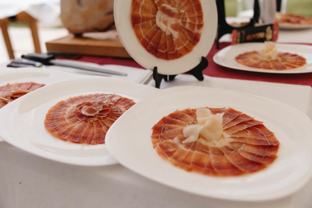 Mesa con varios platos de jamón ibérico recién emplatados, con el jamonero al fondo
